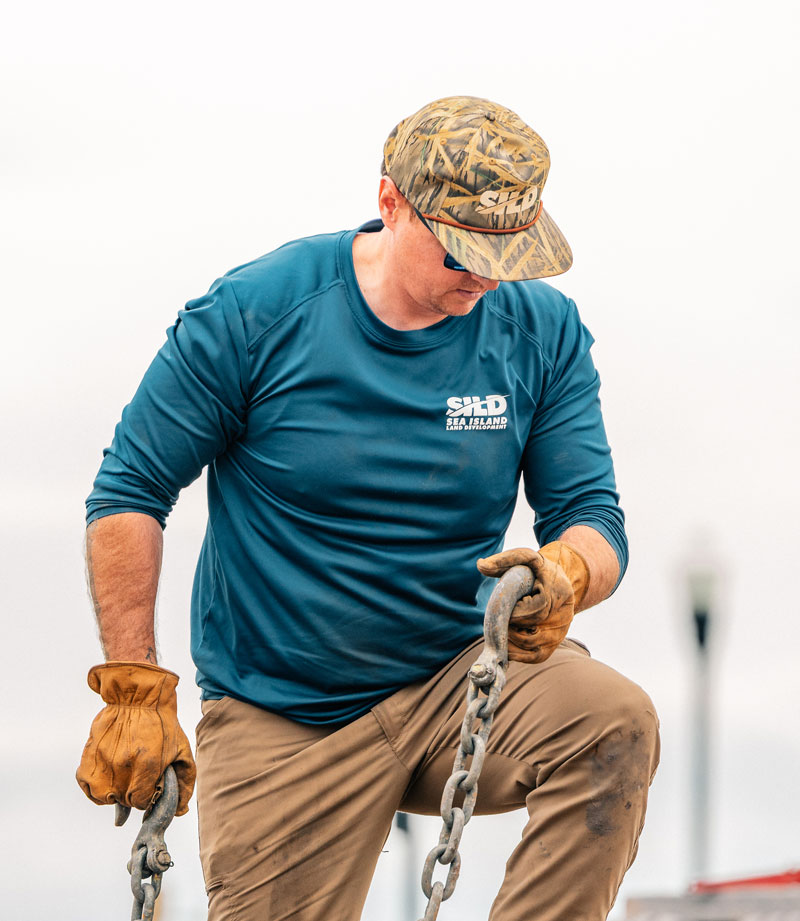 Construction worker securing heavy-duty rigging chains on sitework machinery.